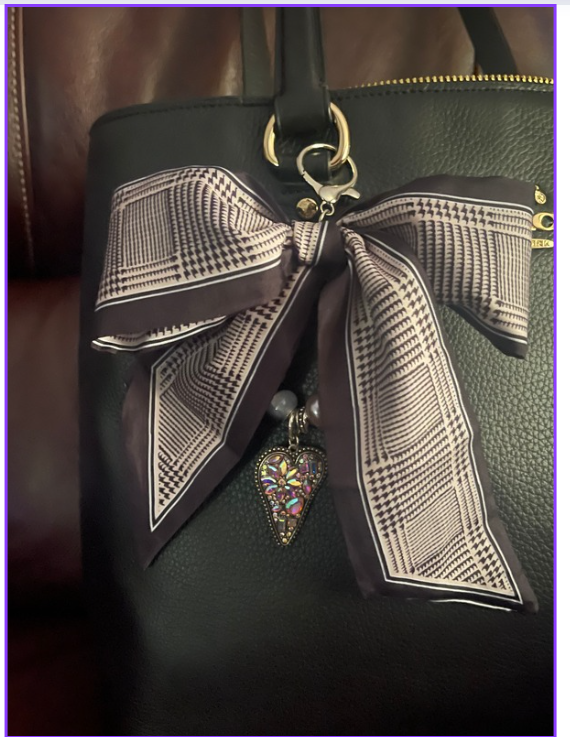 Black and ivory check-patterned bow bag charm with a colorful dangling heart accent on a black handbag