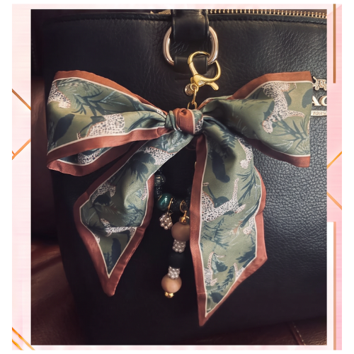 Olive green botanical patterned bow bag charm with rust-colored trim and dangling beads on a black handbag
