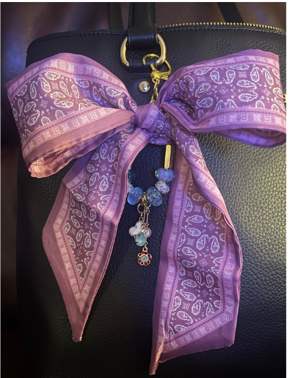 Purple and mauve paisley bow bag charm with blue and lavender beads on a black handbag
