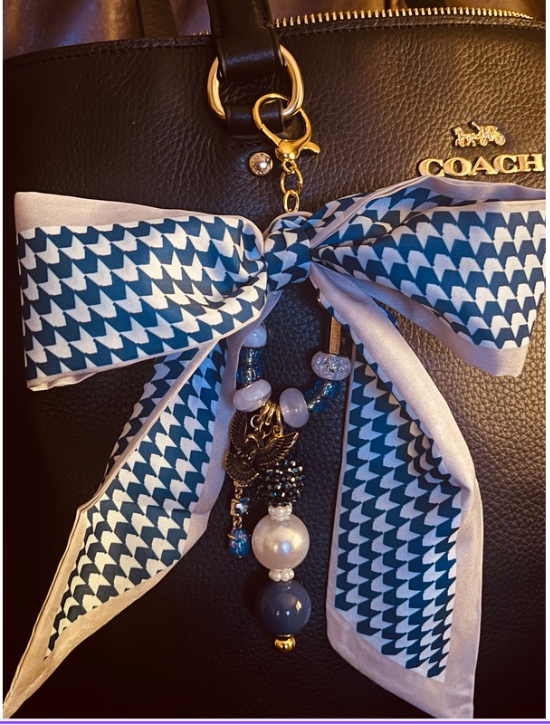 Blue and white geometric bow bag charm with dangling blue and pearl-look beads on a black handbag