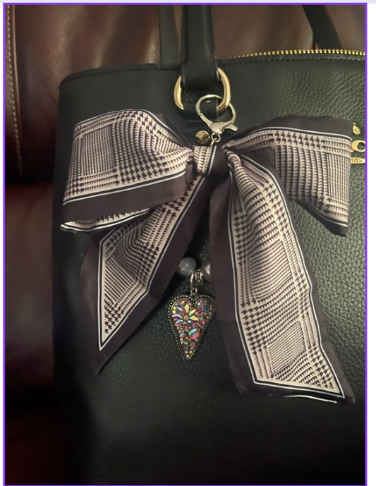 Black and ivory check-patterned bow bag charm with a colorful dangling heart accent on a black handbag